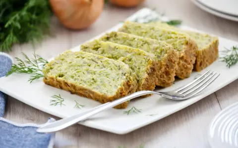 Fette di flan di zucchine su un piatto bianco, guarnite con aneto. Una forchetta argentata è appoggiata sul piatto.