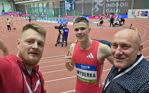 Trzej mężczyźni na bieżni lekkoatletycznej. W środku zawodnik Maciej Wyderka w stroju sportowym.