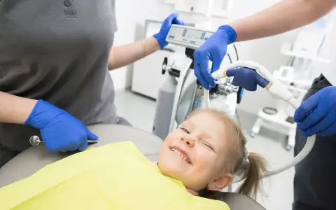 Uśmiechnięta dziewczynka na fotelu dentystycznym, przygotowywana do zabiegu z użyciem sedacji wziewnej.