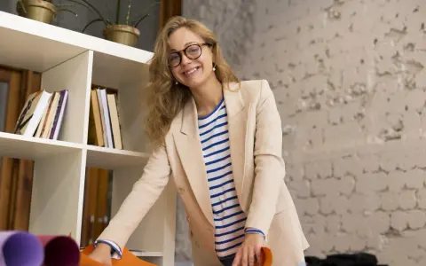 Uśmiechnięta kobieta w beżowej marynarce i pasiastym T-shircie, z okularami na nosie. Jej strój to przykład profesjonalnego dress code nauczyciela.