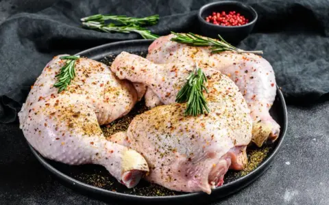 Quatre cuisses de poulet crues, assaisonnées et garnies de romarin, prêtes pour une marinade poulet savoureuse.