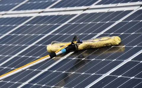 Reinigung von Solaranlagen mit einem Teleskopwischer. Gelber Wischerkopf auf dunklen Solarzellen.