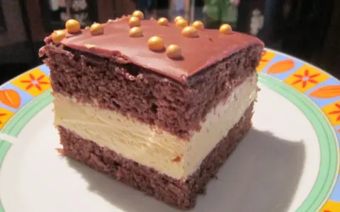 Pyszne milky way ciasto z czekoladowym blatem i kremowym nadzieniem, ozdobione złotymi kuleczkami.