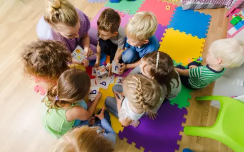 Dzieci i nauczycielka bawią się kartami z literami, ucząc się alfabetu. Ciekawe zajęcia w przedszkolu.