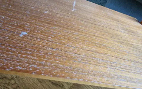 Detaljerad bild av en sliten teakskiva, redo för att renovera teakbord. Vita fläckar och repor syns tydligt.
