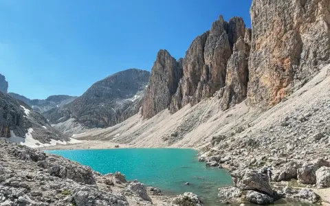 Il **lago di Antermoia**, incastonato tra imponenti pareti rocciose, brilla di un turchese intenso sotto un cielo azzurro.