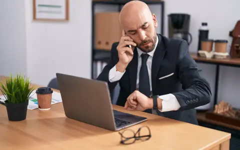 Zmęczony biznesmen sprawdza zegarek, zastanawiając się nad wymiarem czasu pracy.