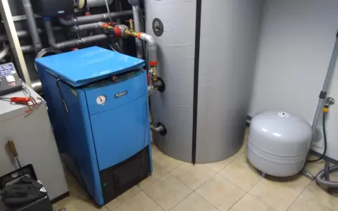 Niebieski bufor do pieca stoi obok dużego, szarego bojlera i mniejszego, białego zbiornika.