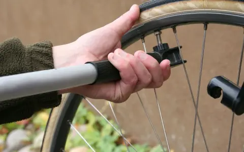 Dłoń trzyma pompkę rowerową, przygotowując się do sprawdzenia, jakie ciśnienie w oponach jest optymalne.
