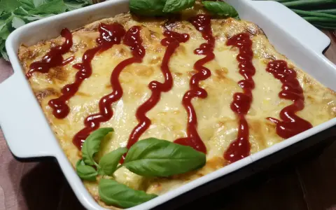 Pyszne, zapieczone fit lasagne w białym naczyniu, polane ketchupem i ozdobione listkami bazylii.