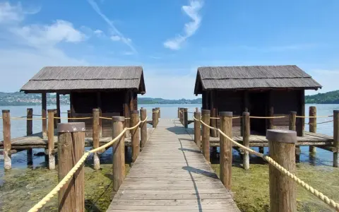 Pontile in legno con due capanne sul lago di Viverone, sotto un cielo azzurro con nuvole bianche.