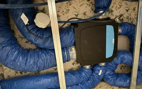 Système de ventilation centralisé avec un boîtier noir et bleu, entouré de conduits bleus isolés. Ce système VMC programmable assure un air sain.