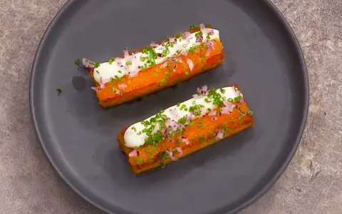 Två gyllene, rektangulära tater tots toppas med gräddfil, finhackad rödlök och gräslök.