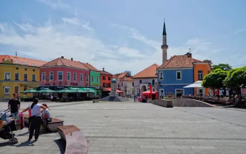 Kolorowy plac w **Tuzla, Bośnia**, z kawiarniami, fontanną i minaretem w tle.