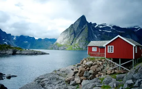 Två röda stugor vid en sjö med dramatiska berg i bakgrunden. Perfekt för att vandra i Norge.