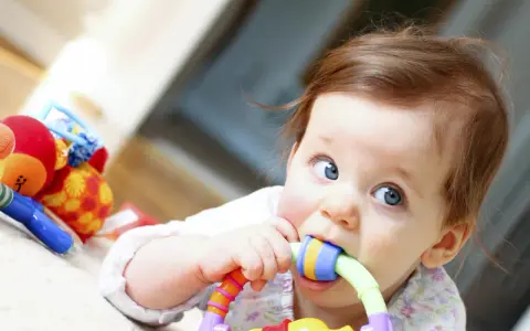 Bébé curieux mordillant un jouet coloré, dans le cadre d'un projet d'accueil individualisé pour son développement.
