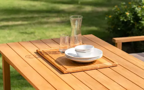Vacker teakmöbel som behöver behandlas för att behålla sin lyster. Tallrikar, skålar och glas står redo för en utomhusmåltid.