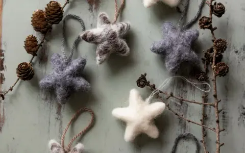 Mjuka, filtade julstjärnor i grått och vitt, som påminner om klassiska julpyssel. Dekorerade med kottar och grenar på en sliten träbakgrund.