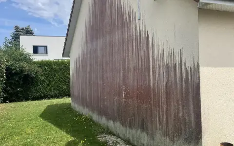 Traces sombres sur un mur extérieur, probablement dues à des algues rouges et à l'eau de javel.