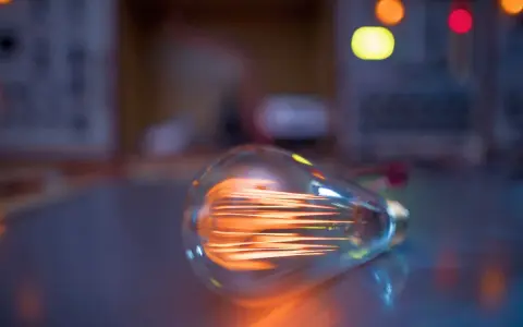 Żarówka LED 8 watt ile to wat? Widoczna żarówka z rozżarzonym żarnikiem, w tle kolorowe światła.