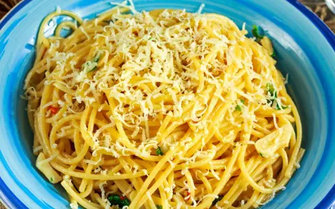 Porcja spaghetti z tartym serem i ziołami w niebieskiej misce.