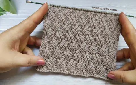 Manos sostienen un tejido cruzado de lana beige con un patrón de rombos entrelazados.