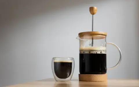 Frisch gebrühter Kaffee mit Wasser in einer French Press und einem Glas. Der Duft von Kaffee liegt in der Luft.