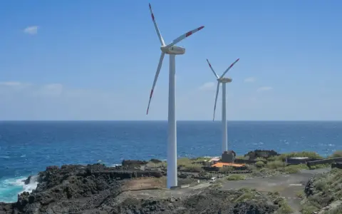 Zwei Windräder an einer felsigen Küste Spaniens, die saubere Energie erzeugen.
