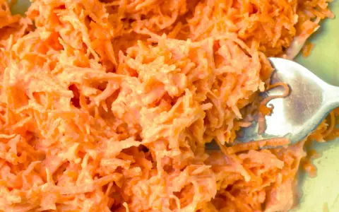 Tarta marchewka z majonezem, idealna jako surówka do obiadu. Widoczna łyżka widelca zagłębia się w pomarańczową masę.