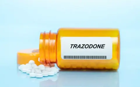 Pomarańczowa butelka leku trazodon, z kilkoma białymi tabletkami rozsypanymi obok.