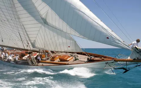 Eine elegante 12mr Yacht gleitet über das türkisfarbene Meer, die weißen Segel strahlen in der Sonne.