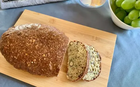 Chleb z twarogu na desce, pokrojony w kromki, obok miseczka z winogronami. Idealny przepis na chleb z twarogu.