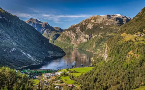 Majestätische norwegen fjorde mit einem Kreuzfahrtschiff, das auf dem ruhigen Wasser fährt. Grüne Berghänge und ein kleines Dorf am Ufer.