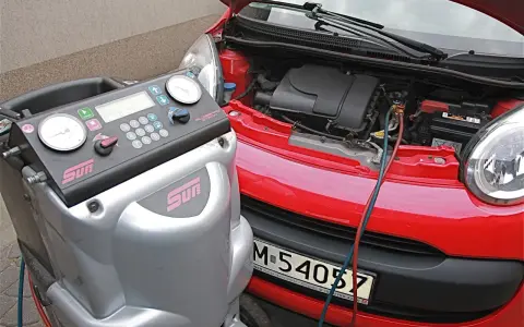 Urządzenie do serwisu klimatyzacji podłączone do czerwonego samochodu. Dowiedz się, ile kosztuje nabicie klimatyzacji.
