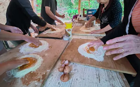Bambini e adulti impastano farina e uova in una fattoria in Abruzzo, un'esperienza culinaria all'aperto.