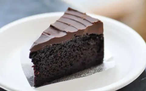 Una fetta di torta al cioccolato senza burro, soffice e ricoperta da glassa al cioccolato, servita su un piatto bianco.
