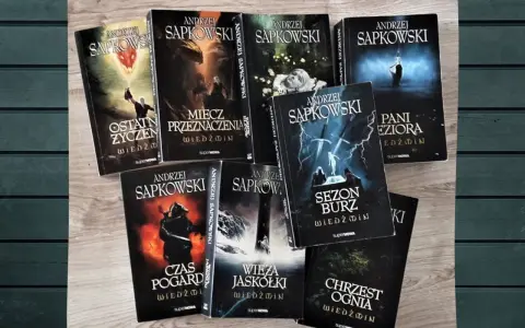 Książki Andrzeja Sapkowskiego z serii Wiedźmin ułożone na drewnianym tle.