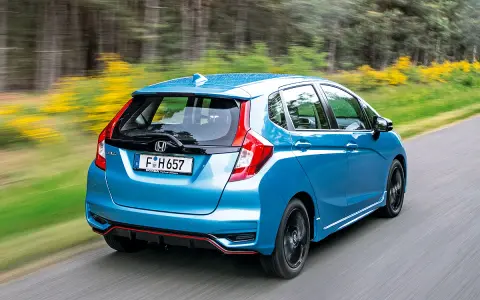 Blauer Honda Jazz Hybrid fährt auf einer Landstraße. Trotz der schönen Fahrt gibt es Berichte über Honda Jazz Hybrid Probleme.