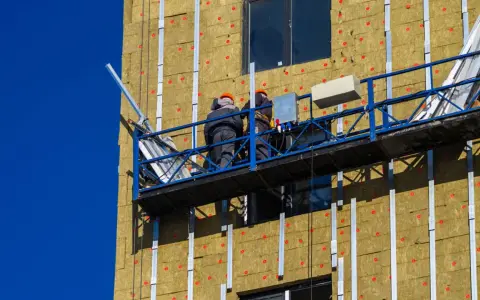Trabajadores en plataforma instalan aislamiento térmico exterior en edificio.