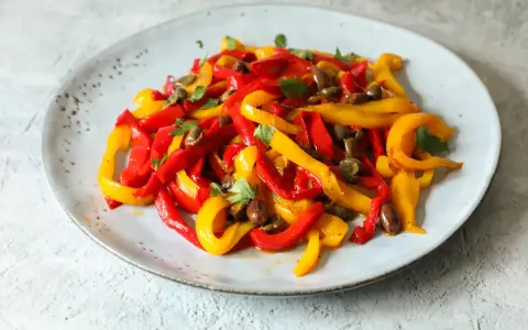 Peperoni in padella, tagliati a listarelle rosse e gialle, conditi con olive e capperi, guarniti con prezzemolo fresco.
