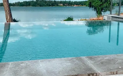 En vacker infinity pool som speglar himlen och omgivande träd. Drömmen om att bygga infinity pool vid en sjö.