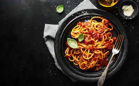 Un piatto di spaghetti alla carrettiera fumanti, conditi con un ricco sugo di pomodoro e basilico fresco, su sfondo scuro.