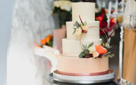 Czteropiętrowy tort weselny w pastelowych kolorach, ozdobiony świeżymi kwiatami i złotym pierścieniem. To najmodniejsze najpiękniejsze torty weselne.