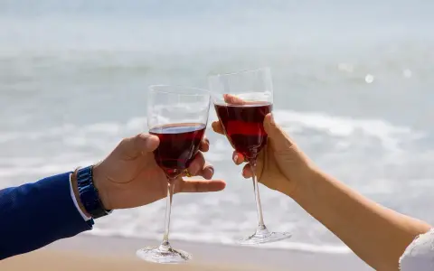 Dwie ręce unoszą kieliszki z czerwonym winem na tle morza. Idealne drinki z winem na romantyczny wieczór.