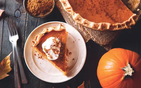 Un trozo de pastel de calabaza con crema batida y canela, junto a una calabaza entera y especias. ¡Deliciosos postres con calabaza!