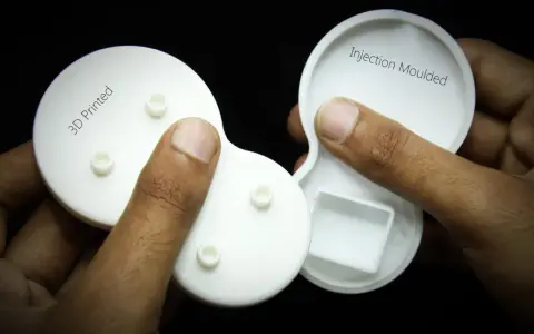 Hands hold two white plastic parts, one labeled "3D Printed" and the other "Injection Moulded," showcasing the difference between the two manufacturing methods.