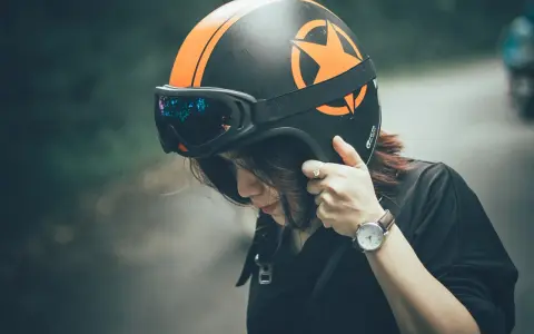 Donna con casco nero e arancione, occhiali riflettenti. Il casco deve calzare bene per la sicurezza.