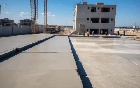 Plac budowy z wylewanym betonem na fundamenty. Widać budynek w stanie surowym, dźwigi i pracowników. Jaki beton na fundament b20 czy b25?