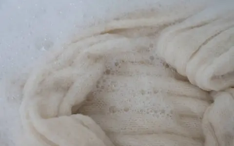 Lana bianca in acqua saponata, un processo che porta all'infeltrimento della lana per creare texture uniche.