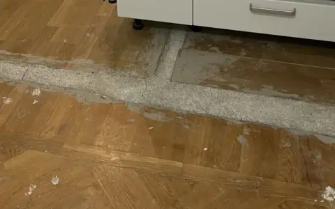 Arbete pågår för att ta bort laminatgolv. Ett vitt pulver och grått material syns på det gamla trägolvet.